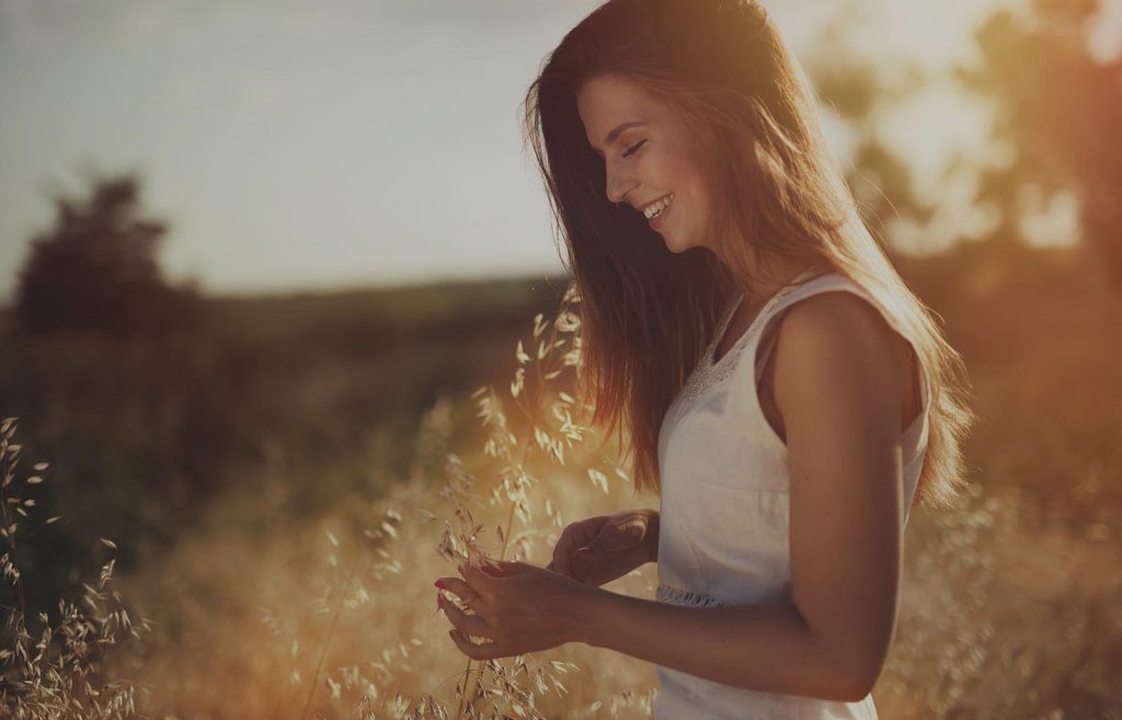 Happy woman smiling in a field at sunset