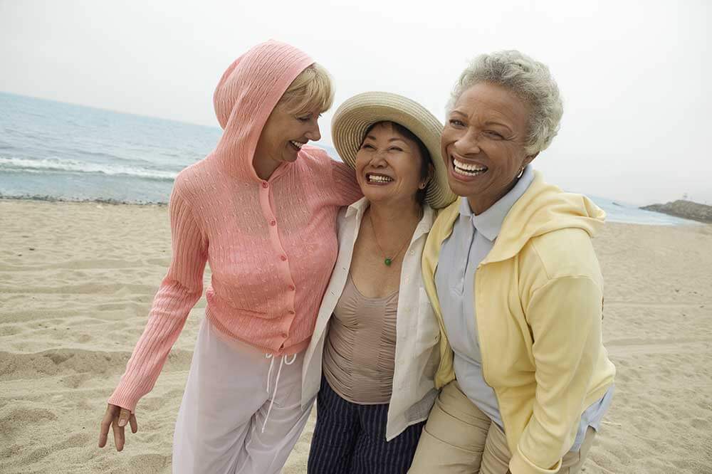three older woman all laughing and smiling at the beach