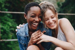 Two girl friends with their arms around each other, smiling and laughing