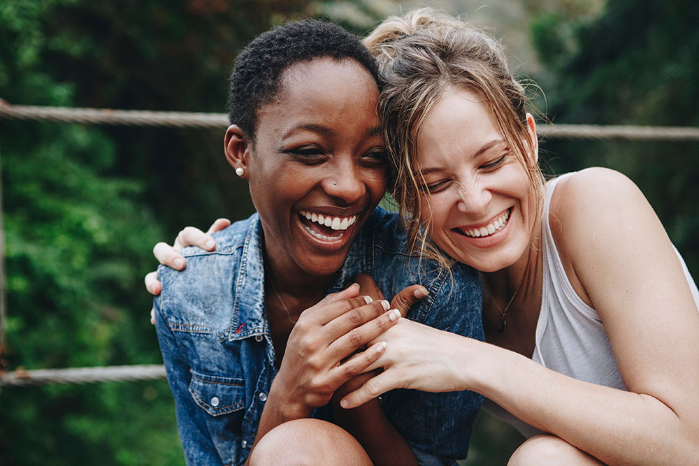 Two girl friends with their arms around each other, smiling and laughing