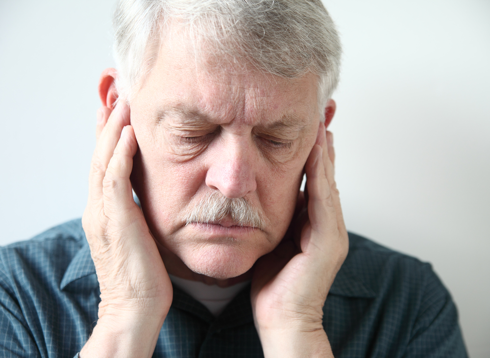 older man with white hair holding his ears due to pain