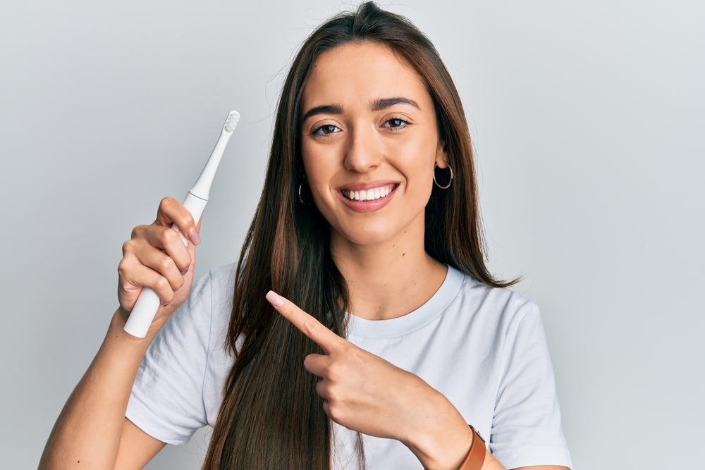 woman holding her electric toothbrush and pointing to it