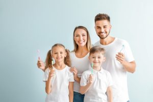 family of four holding up dental products and smiling