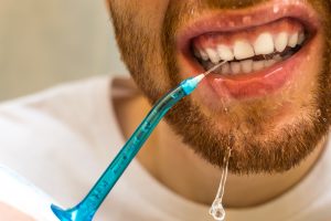 up close view of a man using a waterpik to clean between his teeth