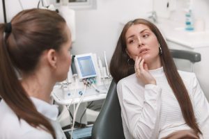 young woman sitting in the dental chair holding her mouth in pain