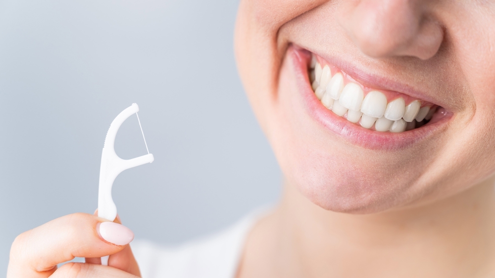 woman smiling while holding a floss pick