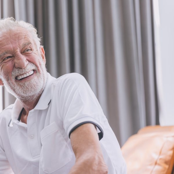 Smiling older man in a white polo shirt, conveying confidence and satisfaction, representing the positive outcomes of dental treatments like bone grafting for implants.